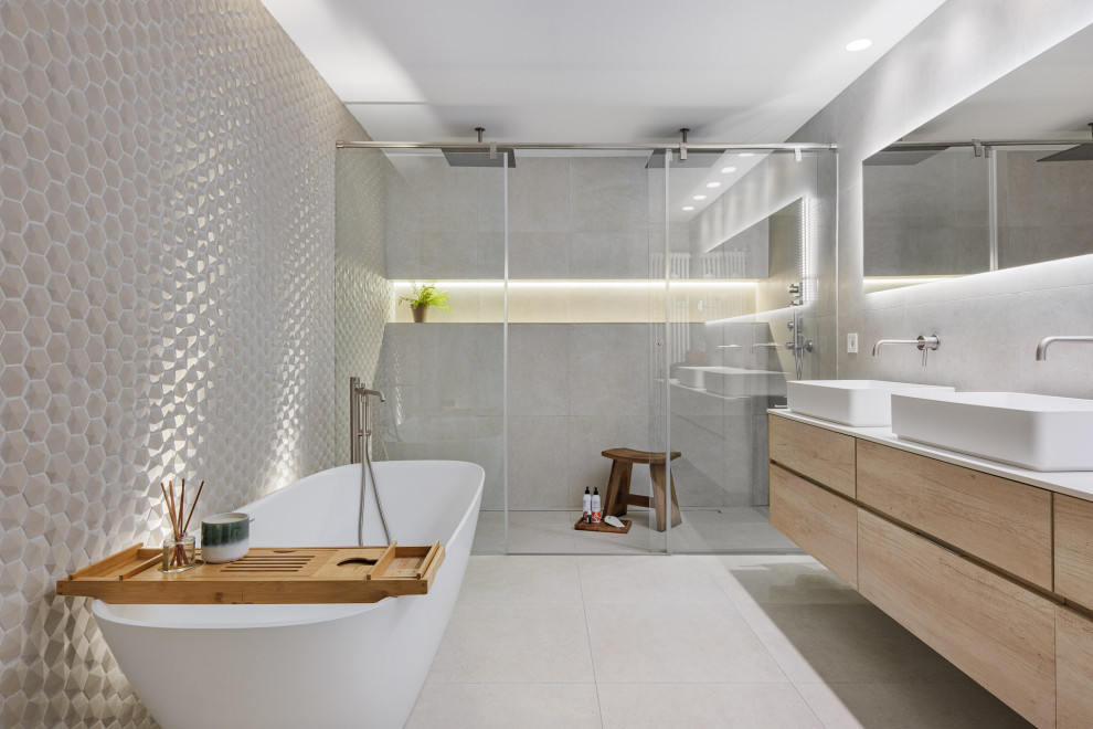 Inspiration för moderna vitt badrum, med släta luckor, skåp i ljust trä, ett fristående badkar, en kantlös dusch, grå kakel, ett fristående handfat, grått golv och dusch med skjutdörr