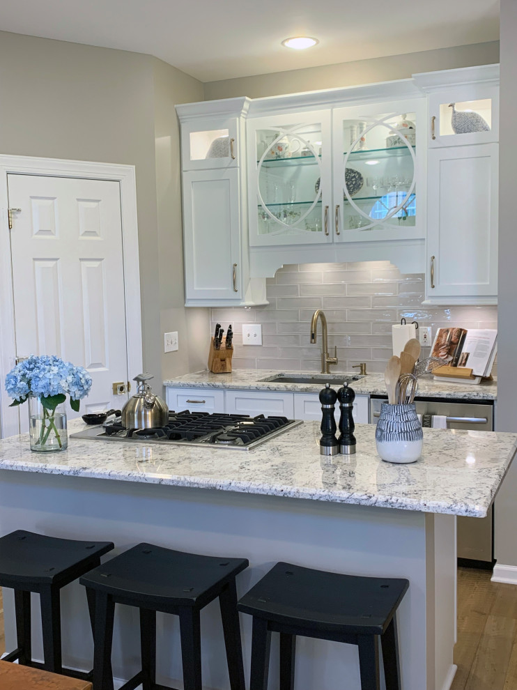 Example of a mid-sized transitional light wood floor and brown floor eat-in kitchen design in DC Metro with an undermount sink, glass-front cabinets, white cabinets, granite countertops, gray backsplash, subway tile backsplash, stainless steel appliances, an island and white countertops