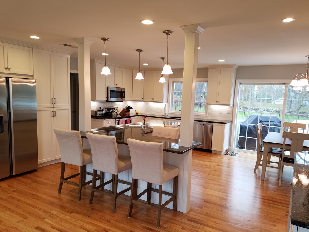 Example of a large transitional l-shaped light wood floor and brown floor eat-in kitchen design with an undermount sink, shaker cabinets, white cabinets, granite countertops, white backsplash, subway tile backsplash, stainless steel appliances and an island