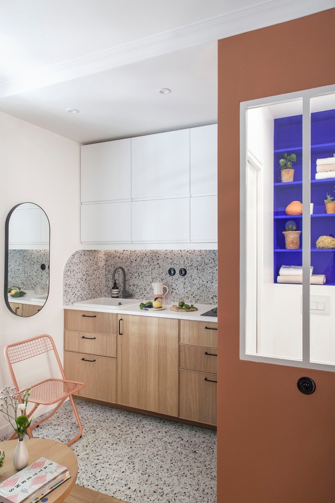 This is an example of a small modern single-wall open plan kitchen in Paris with a single-bowl sink, beaded inset cabinets, light wood cabinets, laminate benchtops, multi-coloured splashback, ceramic splashback, panelled appliances, terrazzo floors, multi-coloured floor and white benchtop.