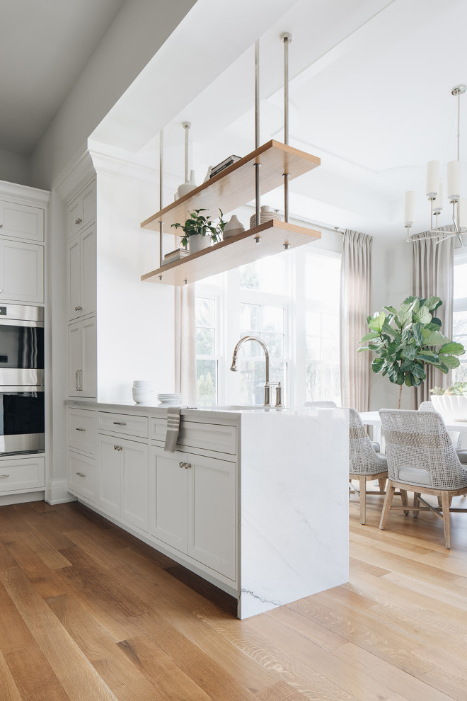 Inspiration for a large transitional eat-in kitchen in Chicago with an undermount sink, beaded inset cabinets, white cabinets, quartz benchtops, stone tile splashback, panelled appliances, light hardwood floors, multiple islands, brown floor and white benchtop.