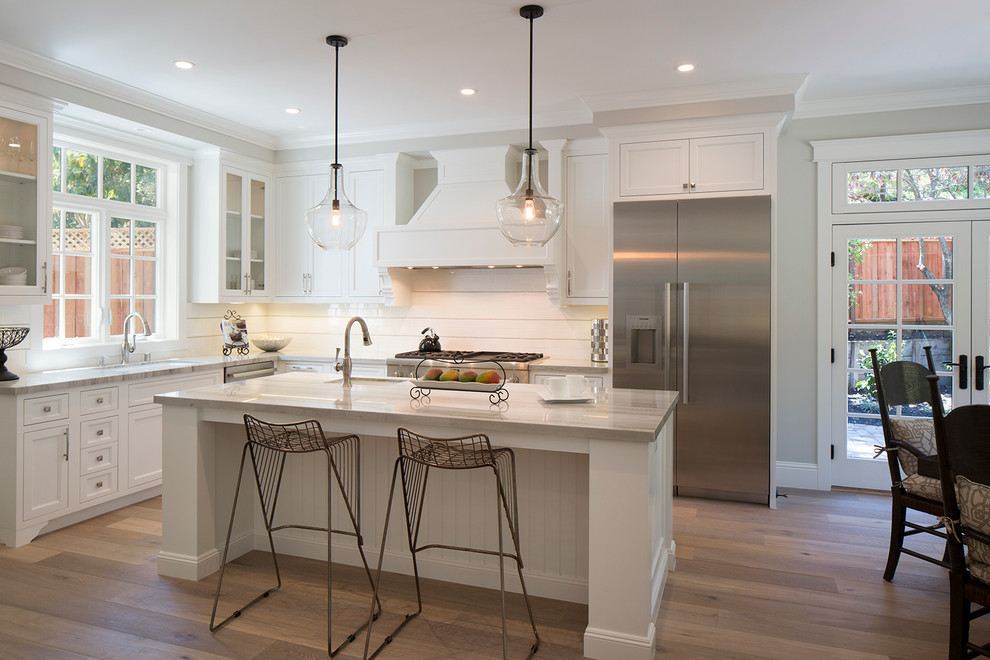 This is an example of a large transitional l-shaped eat-in kitchen in San Francisco with recessed-panel cabinets, white cabinets, stainless steel appliances, medium hardwood floors and with island.