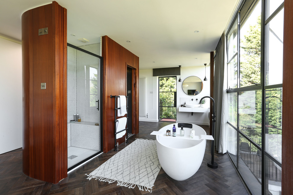 Photo of a mid-sized contemporary master wet room bathroom in London with a freestanding tub, a wall-mount toilet, white tile, porcelain tile, grey walls, dark hardwood floors, a wall-mount sink, quartzite benchtops, brown floor, a hinged shower door and white benchtops.