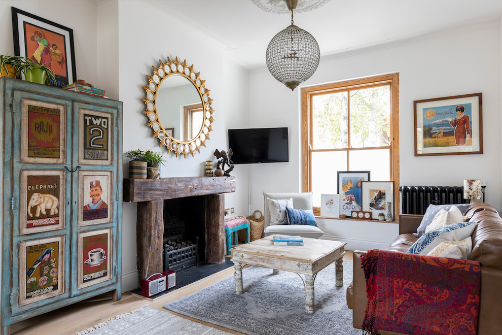 Eclectic enclosed living room in London with white walls, light hardwood floors, a standard fireplace, a wood fireplace surround and a wall-mounted tv.