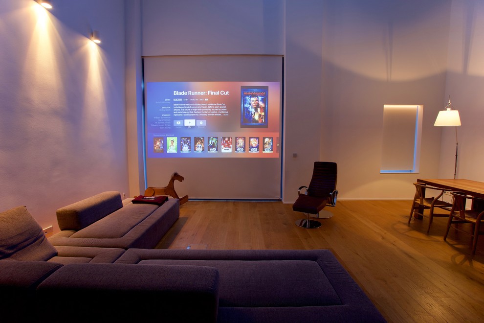Photo of a large modern open concept home theatre in Dusseldorf with white walls, light hardwood floors, a projector screen and yellow floor.