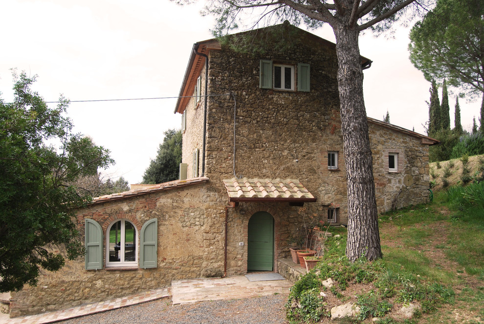 Design ideas for a mid-sized country three-storey beige exterior in Milan with stone veneer and a gable roof.
