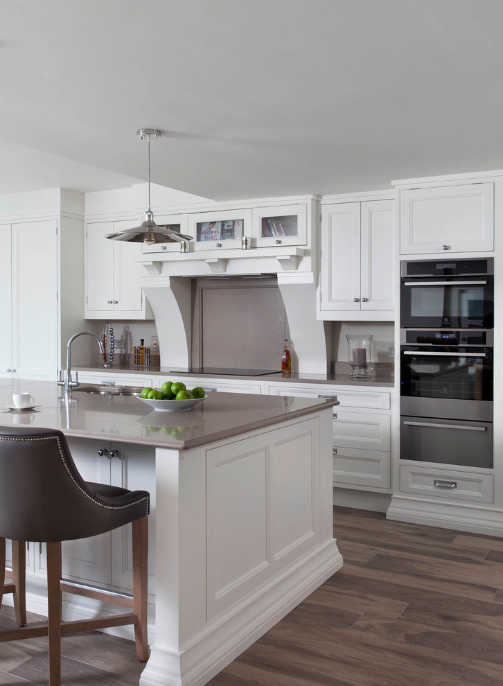 Design ideas for a large traditional single-wall open plan kitchen in Other with an integrated sink, beaded inset cabinets, white cabinets, quartzite benchtops, brown splashback, stone slab splashback, stainless steel appliances, medium hardwood floors, with island and brown floor.