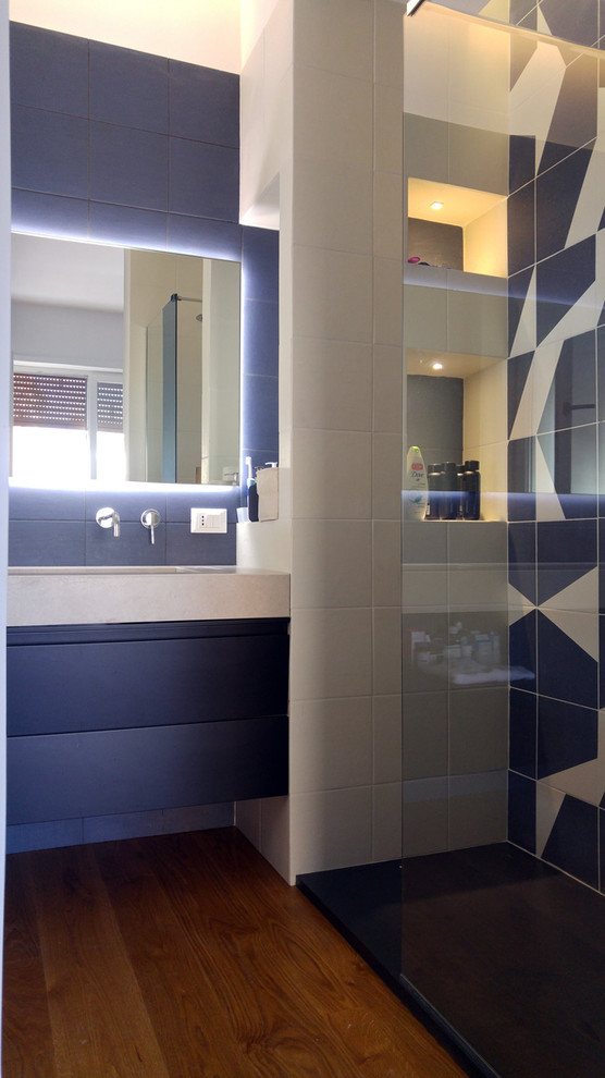This is an example of a contemporary bathroom in Rome with beige cabinets, a wall-mount toilet, blue tile, porcelain tile, medium hardwood floors, an integrated sink and concrete benchtops.