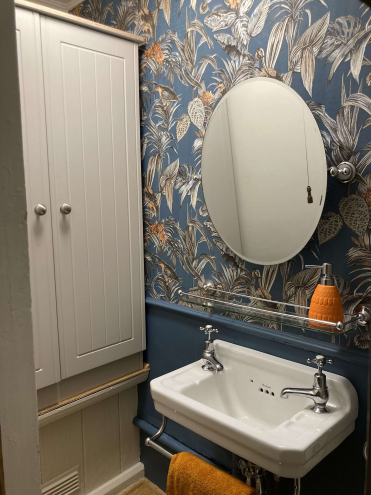 Cette photo montre un petit WC et toilettes victorien avec WC à poser, un mur bleu, sol en stratifié, un lavabo suspendu, un sol marron et du papier peint.