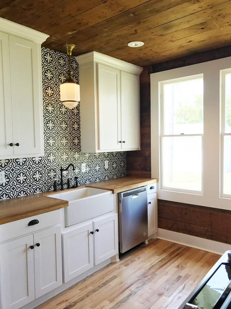 Photo of a mid-sized country kitchen in Dallas with cement tile splashback, a farmhouse sink, shaker cabinets, white cabinets, wood benchtops, stainless steel appliances, cement tiles, with island and brown floor.