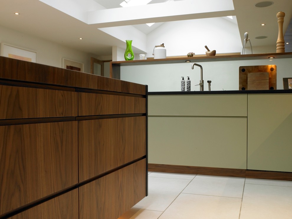 This is an example of a mid-sized contemporary open plan kitchen in London with an integrated sink, flat-panel cabinets, green cabinets, granite benchtops, glass sheet splashback, stainless steel appliances, porcelain floors and with island.