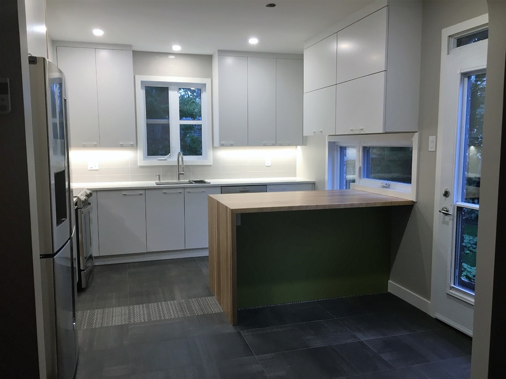 This is an example of a mid-sized contemporary l-shaped kitchen pantry in Montreal with an undermount sink, flat-panel cabinets, white cabinets, wood benchtops, grey splashback, ceramic splashback, stainless steel appliances, porcelain floors, with island and grey floor.