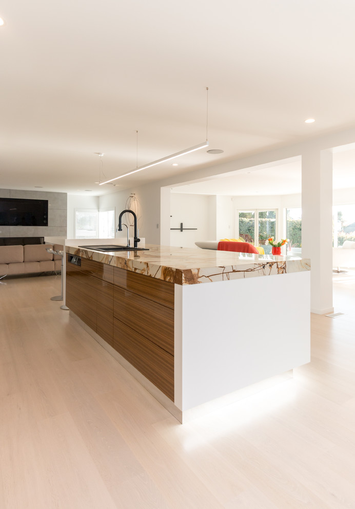 Expansive modern galley open plan kitchen in Auckland with a double-bowl sink, white cabinets, quartzite benchtops, green splashback, glass sheet splashback, white appliances, light hardwood floors and with island.