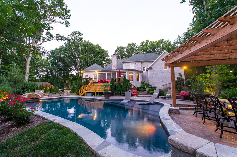 This is an example of a large backyard custom-shaped natural pool in Nashville with a water feature and concrete pavers.