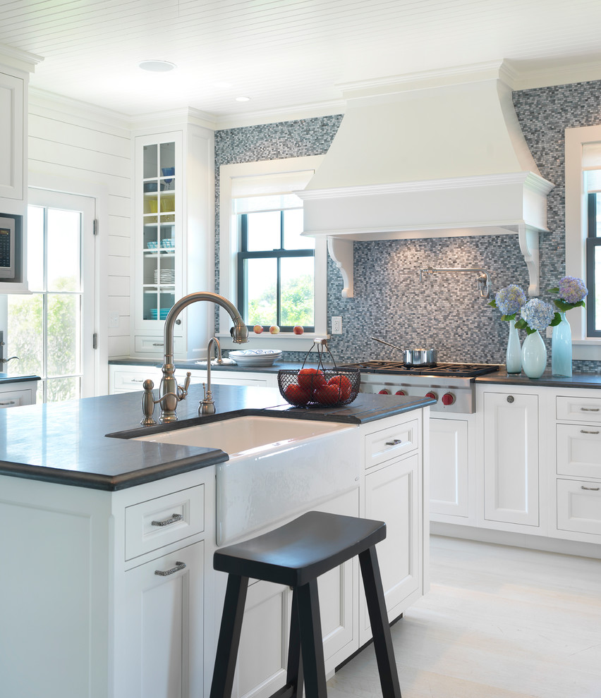 This is an example of a beach style kitchen in Boston with a farmhouse sink, recessed-panel cabinets, white cabinets, wood benchtops, grey splashback, mosaic tile splashback and stainless steel appliances.