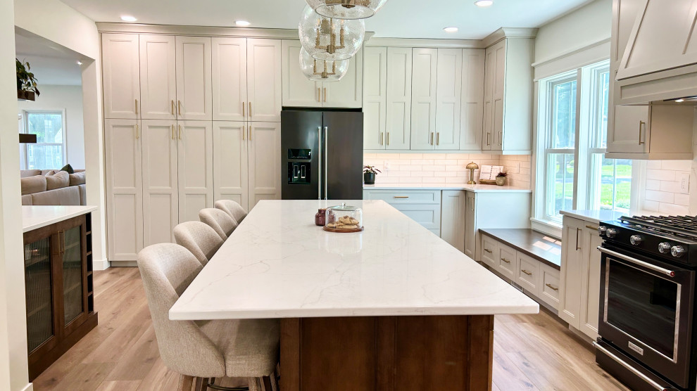 Example of a large transitional u-shaped light wood floor open concept kitchen design with an undermount sink, flat-panel cabinets, white cabinets, quartz countertops, white backsplash, ceramic backsplash, black appliances, an island and white countertops