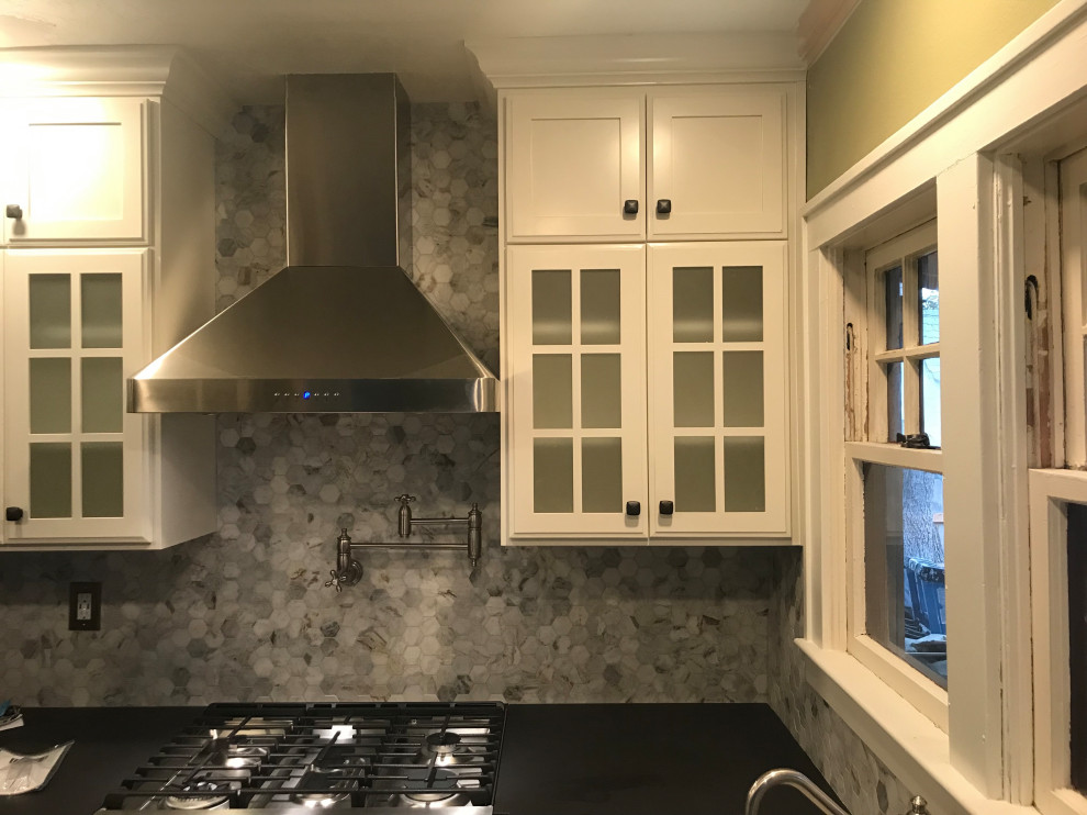 This is an example of a small traditional l-shaped eat-in kitchen in Portland with an undermount sink, glass-front cabinets, white cabinets, quartzite benchtops, grey splashback, stone tile splashback, stainless steel appliances, vinyl floors, a peninsula, black floor and black benchtop.