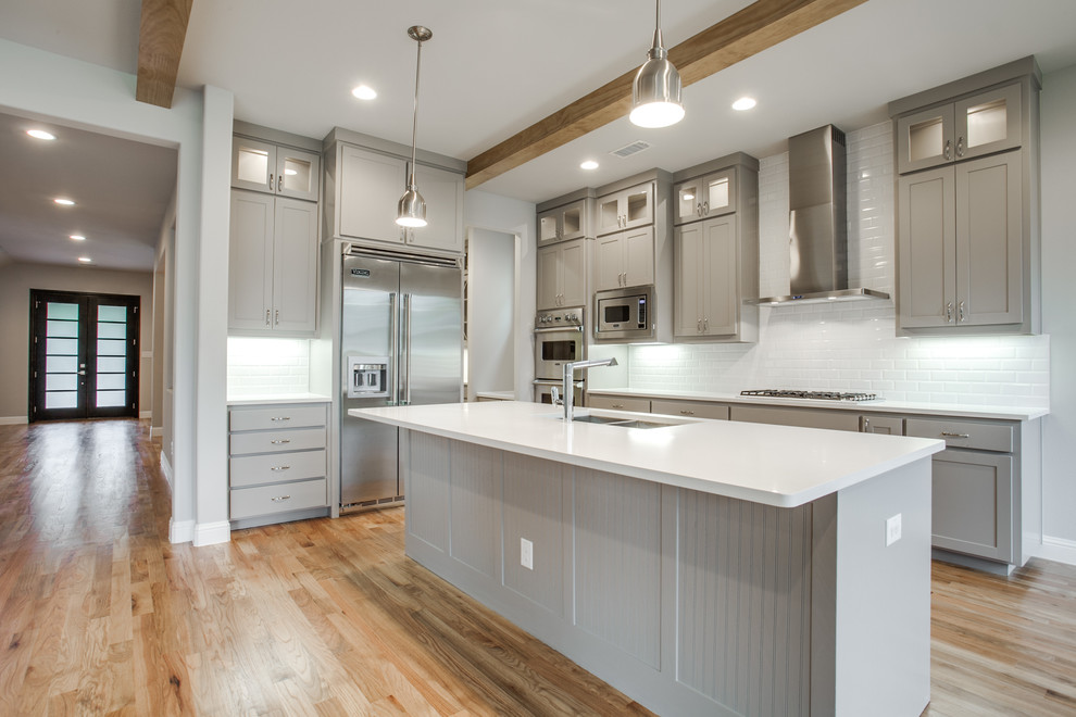 This is an example of a mid-sized transitional l-shaped kitchen in Dallas with an undermount sink, shaker cabinets, grey cabinets, quartz benchtops, white splashback, subway tile splashback, stainless steel appliances, light hardwood floors, with island and brown floor.
