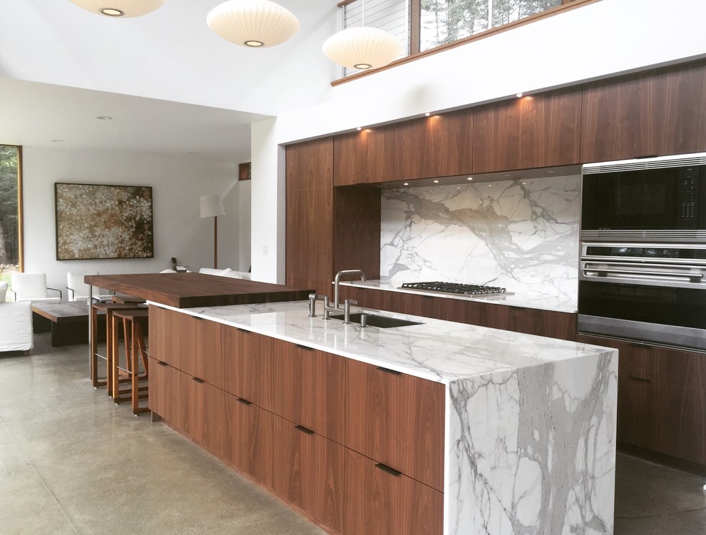 Large contemporary open plan kitchen in New York with an undermount sink, flat-panel cabinets, brown cabinets, marble benchtops, white splashback, stone slab splashback, stainless steel appliances, concrete floors and with island.