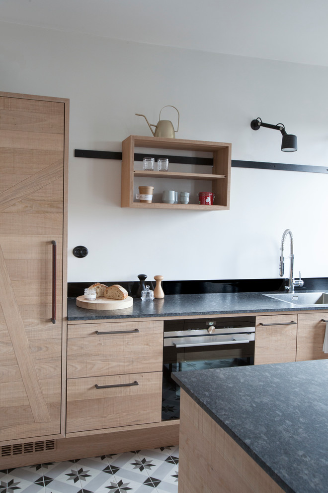 This is an example of a mid-sized industrial galley kitchen in Stockholm with shaker cabinets, light wood cabinets, limestone benchtops, stainless steel appliances, cement tiles, with island and grey benchtop.