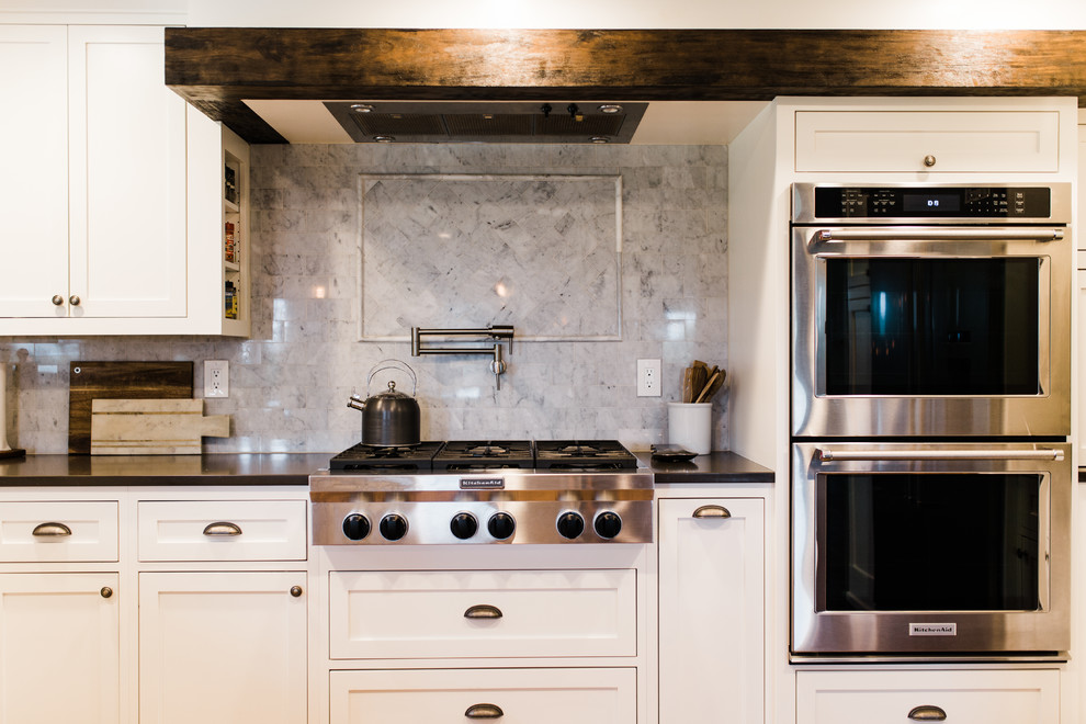 Large transitional u-shaped medium tone wood floor and brown floor eat-in kitchen photo in Phoenix with a farmhouse sink, shaker cabinets, white cabinets, quartzite countertops, gray backsplash, marble backsplash, stainless steel appliances and a peninsula
