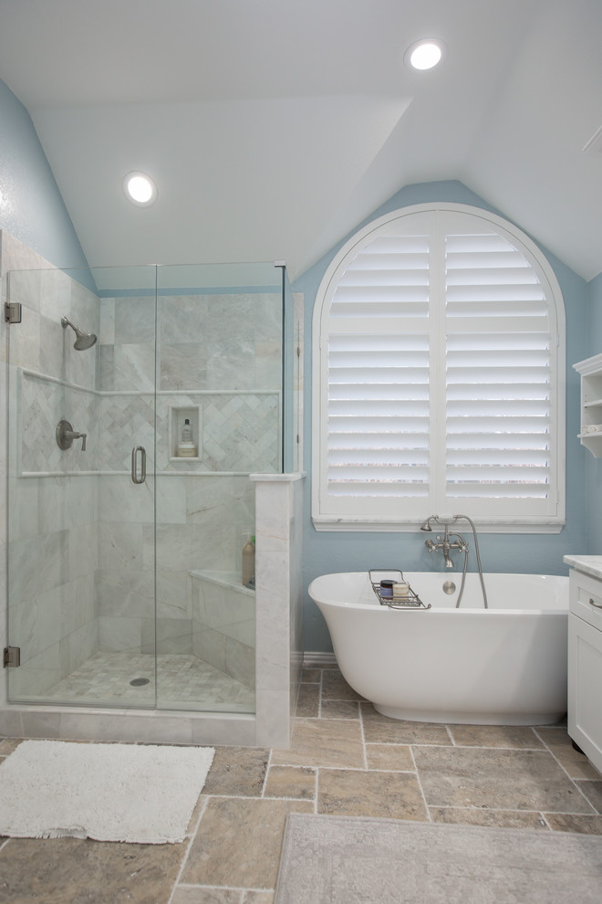 Inspiration for a large beach style master bathroom in Dallas with shaker cabinets, white cabinets, a freestanding tub, a corner shower, gray tile, porcelain tile, blue walls, ceramic floors, an undermount sink, marble benchtops, beige floor, a hinged shower door and white benchtops.