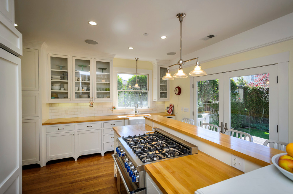 This is an example of an arts and crafts separate kitchen in San Francisco with glass-front cabinets, panelled appliances, subway tile splashback and wood benchtops.