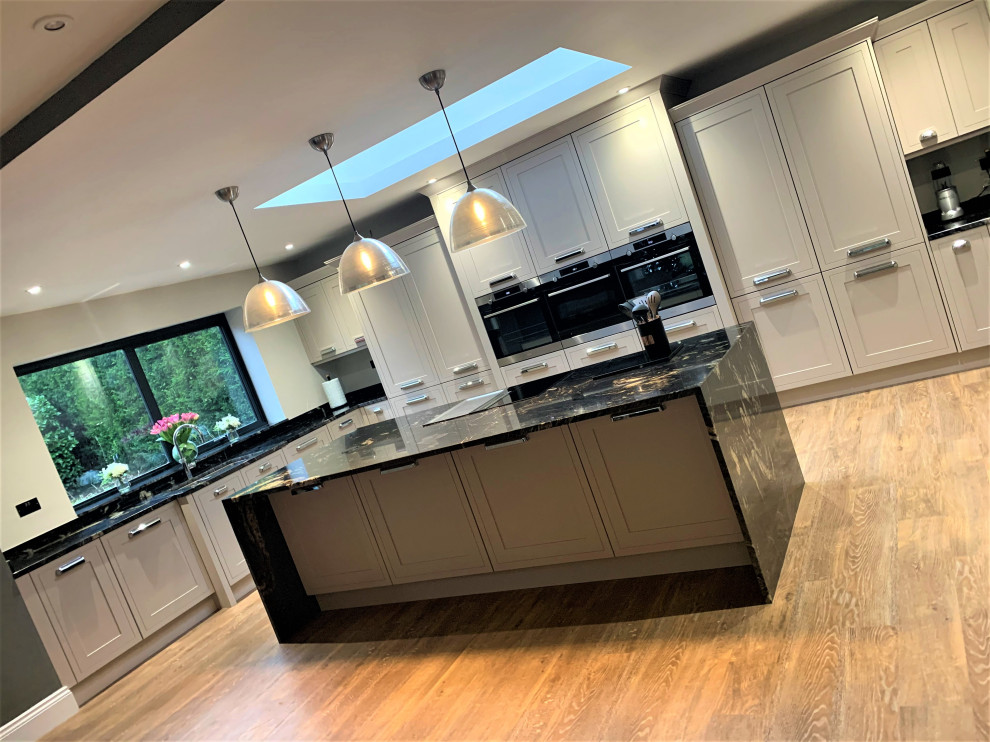 Large traditional u-shaped open plan kitchen in Other with a double-bowl sink, shaker cabinets, medium wood cabinets, granite benchtops, black splashback, black appliances, vinyl floors, with island and black benchtop.