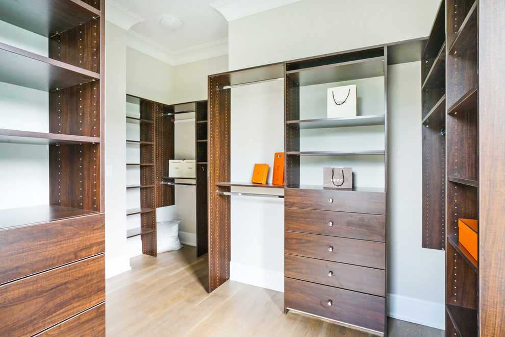 Photo of a mid-sized transitional gender-neutral walk-in wardrobe in New York with flat-panel cabinets, dark wood cabinets, light hardwood floors and brown floor.
