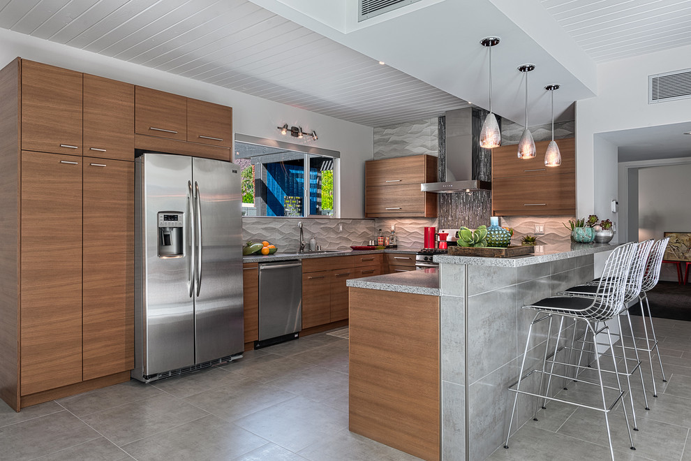 Photo of a midcentury u-shaped kitchen in Los Angeles with flat-panel cabinets, medium wood cabinets, grey splashback, stainless steel appliances, a peninsula and grey floor.