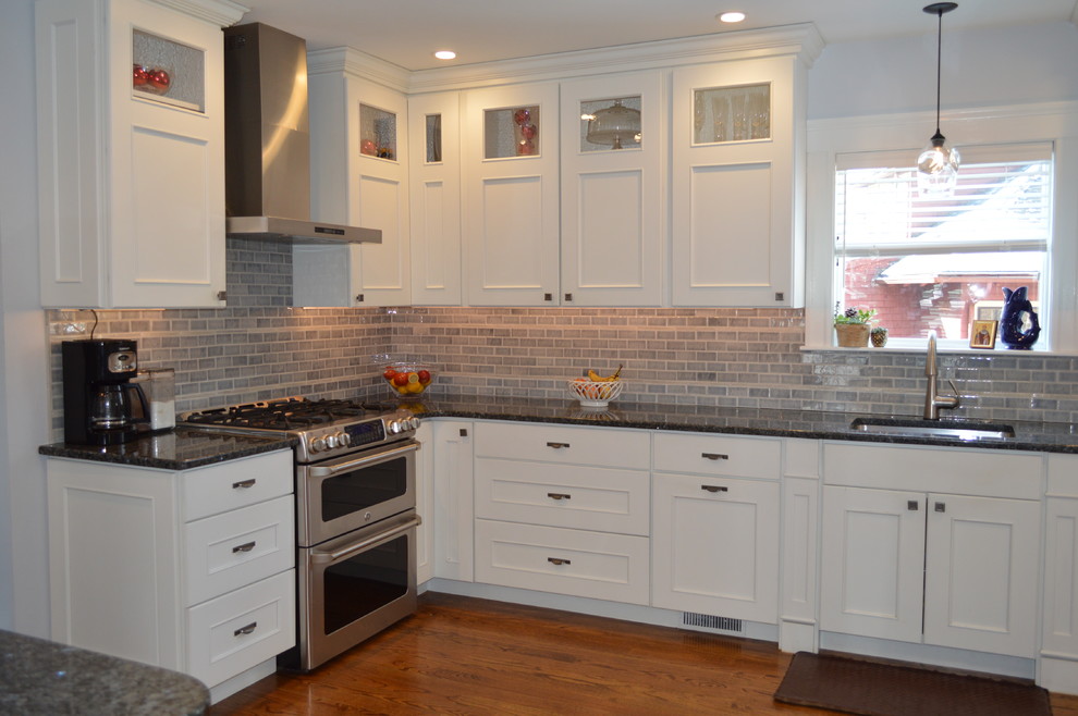 Inspiration for a mid-sized transitional l-shaped medium tone wood floor eat-in kitchen remodel in Boston with an undermount sink, recessed-panel cabinets, white cabinets, granite countertops, gray backsplash, cement tile backsplash, stainless steel appliances, a peninsula and blue countertops