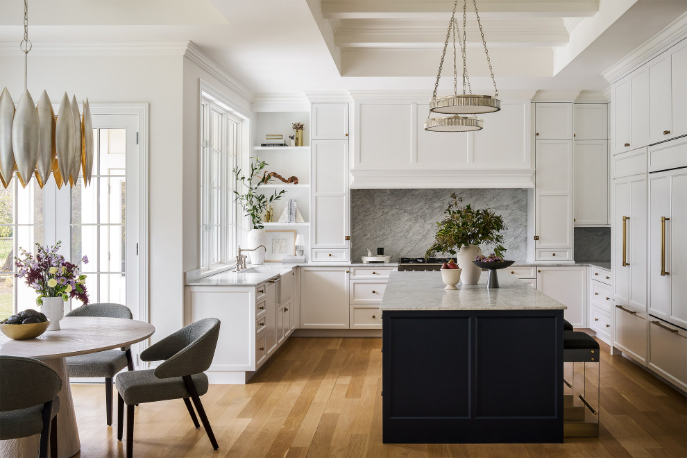 Klassisk inredning av ett grå grått u-kök, med en rustik diskho, luckor med infälld panel, vita skåp, grått stänkskydd, stänkskydd i sten, integrerade vitvaror, mellanmörkt trägolv, en köksö och brunt golv