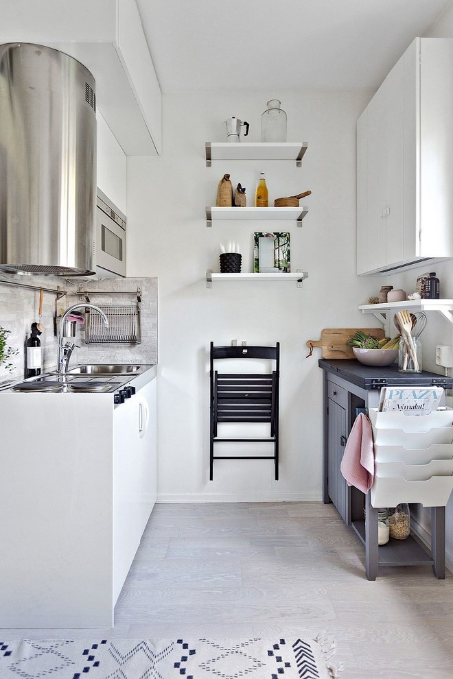 Small scandinavian galley kitchen in Stockholm with a drop-in sink, flat-panel cabinets, white cabinets, grey splashback, stainless steel appliances, light hardwood floors and no island.
