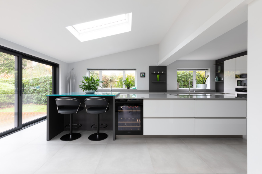 Large contemporary open plan kitchen in Sussex with flat-panel cabinets, white cabinets, composite countertops, grey splashback, an island and grey worktops.