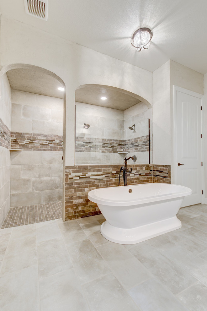 This is an example of a large mediterranean master bathroom in Dallas with raised-panel cabinets, distressed cabinets, a freestanding tub, a double shower, brown tile, matchstick tile, beige walls, an undermount sink, granite benchtops, grey floor, an open shower and beige benchtops.