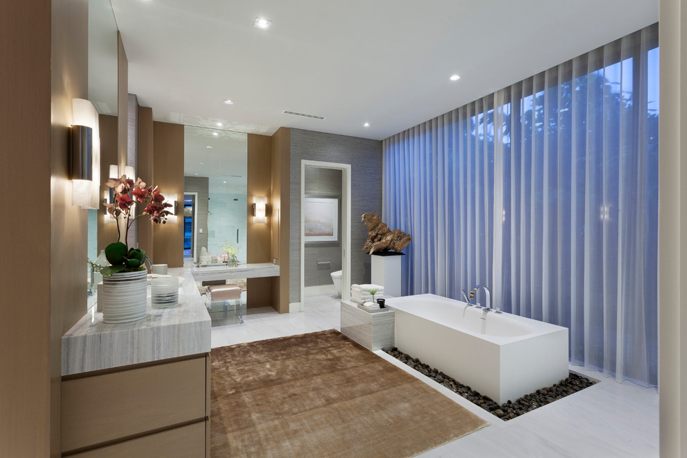 Photo of a large contemporary master bathroom in Miami with flat-panel cabinets, light wood cabinets, an alcove shower, a one-piece toilet, white tile, an undermount sink, marble benchtops, a freestanding tub and brown walls.