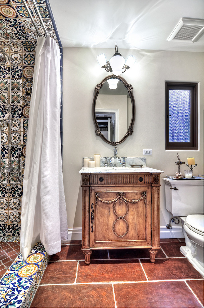 This is an example of a mid-sized mediterranean 3/4 bathroom in Orange County with raised-panel cabinets, medium wood cabinets, a corner tub, a curbless shower, a one-piece toilet, multi-coloured tile, mosaic tile, grey walls, light hardwood floors, an undermount sink and granite benchtops.