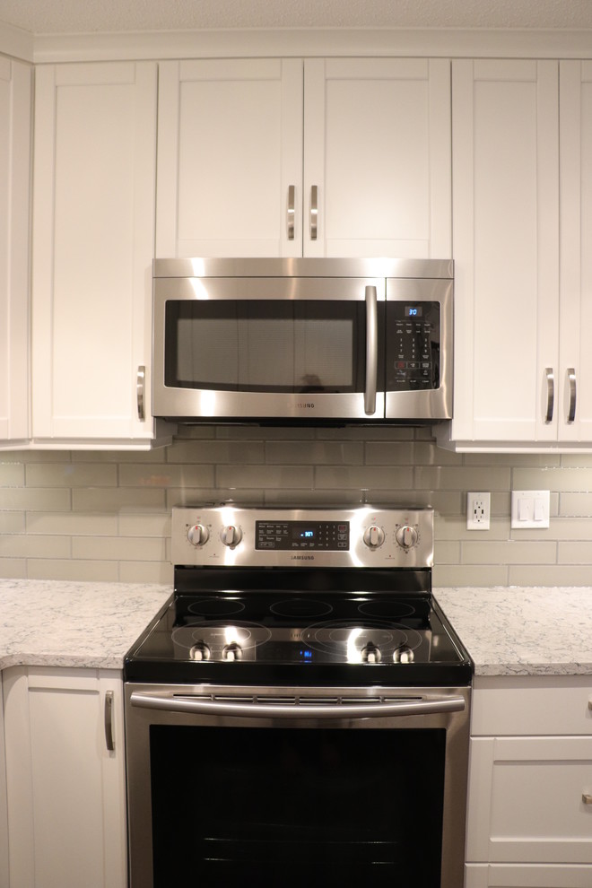 Eat-in kitchen - small transitional u-shaped eat-in kitchen idea in Edmonton with an undermount sink, recessed-panel cabinets, white cabinets, quartz countertops, gray backsplash, glass tile backsplash, stainless steel appliances, no island and white countertops