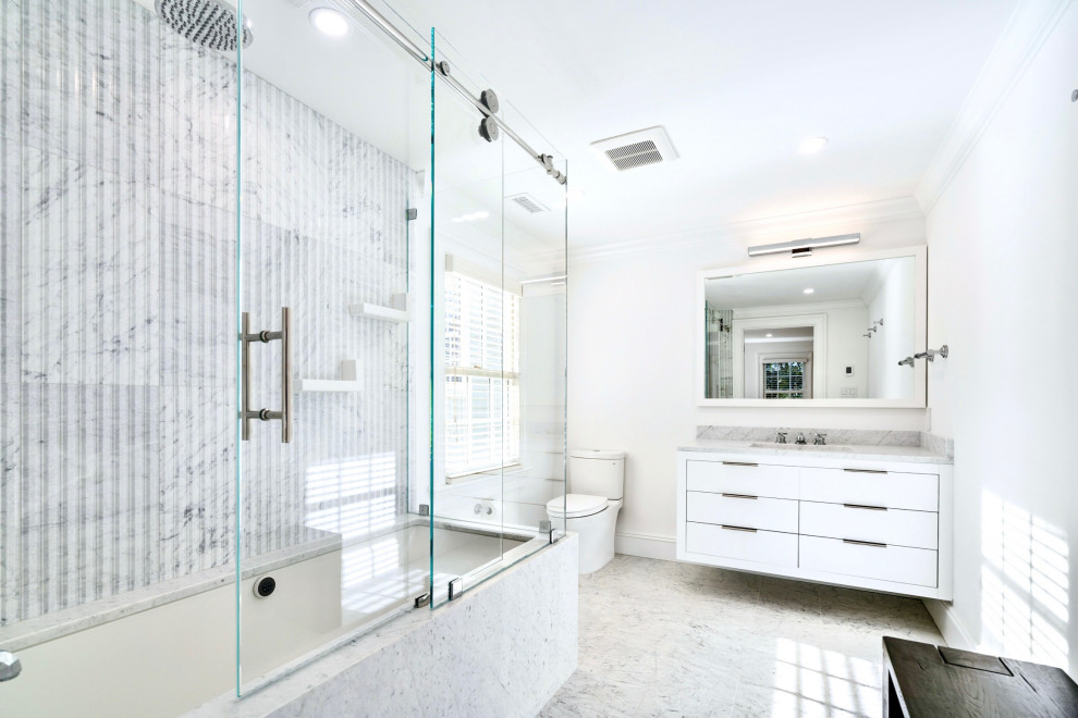 Photo of a mid-sized contemporary master bathroom in Boston with white cabinets, marble, white walls, flat-panel cabinets, an undermount tub, a shower/bathtub combo, a one-piece toilet, white tile, marble floors, an undermount sink, granite benchtops, grey floor, a sliding shower screen, grey benchtops, a single vanity and a floating vanity.