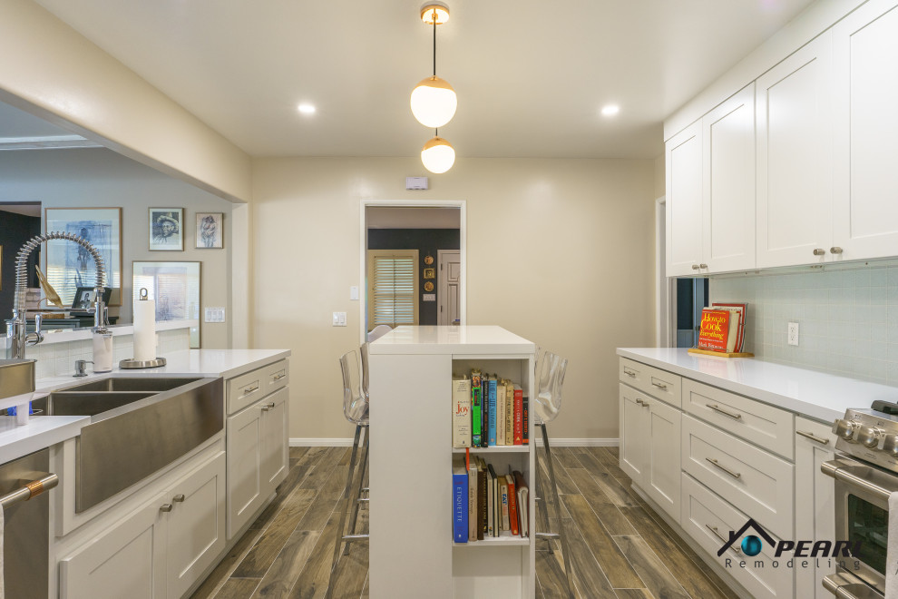Large modern u-shaped eat-in kitchen in Los Angeles with a farmhouse sink, shaker cabinets, white cabinets, solid surface benchtops, white splashback, stone tile splashback, stainless steel appliances, light hardwood floors, with island, brown floor and white benchtop.