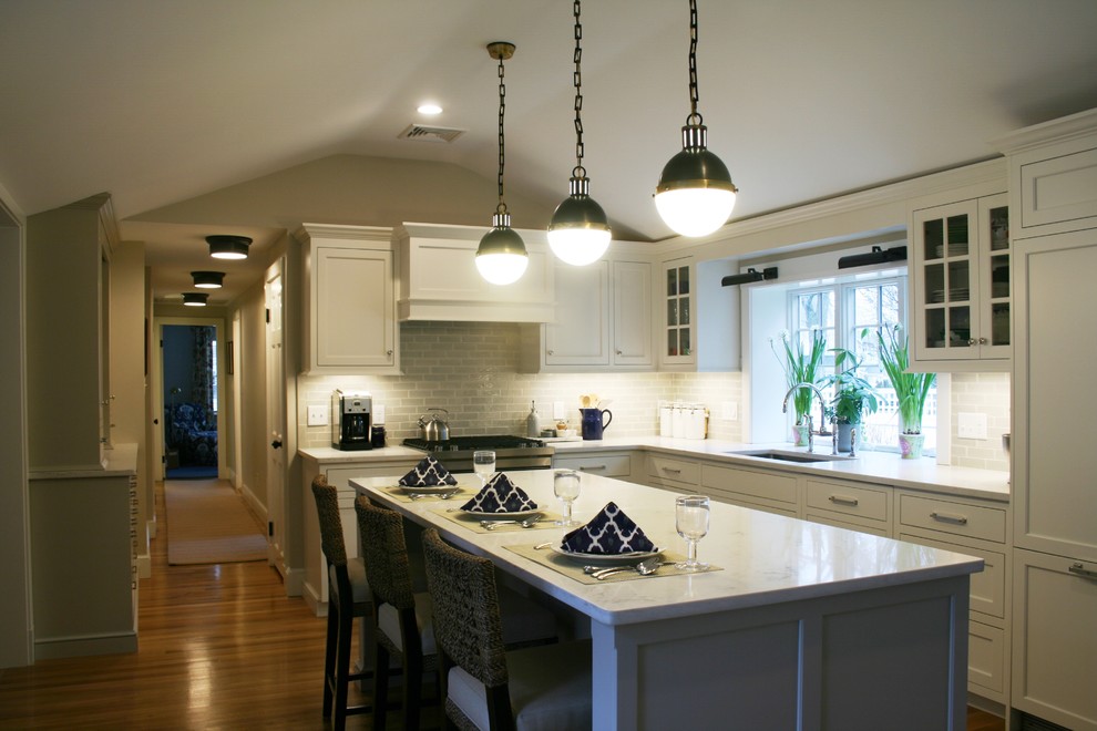 Photo of a mid-sized transitional l-shaped eat-in kitchen in Boston with an undermount sink, shaker cabinets, white cabinets, grey splashback, subway tile splashback, panelled appliances, medium hardwood floors and with island.