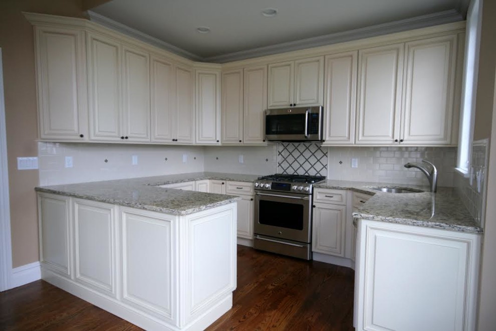 Photo of a traditional u-shaped kitchen in New York with an undermount sink, raised-panel cabinets, white cabinets, granite benchtops, white splashback and stainless steel appliances.