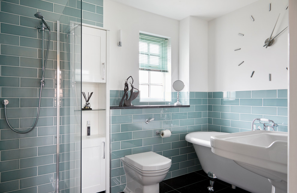 Photo of a mid-sized transitional master bathroom in Surrey with a claw-foot tub, a corner shower, a wall-mount toilet, blue tile, glass tile, white walls, a pedestal sink and black floor.