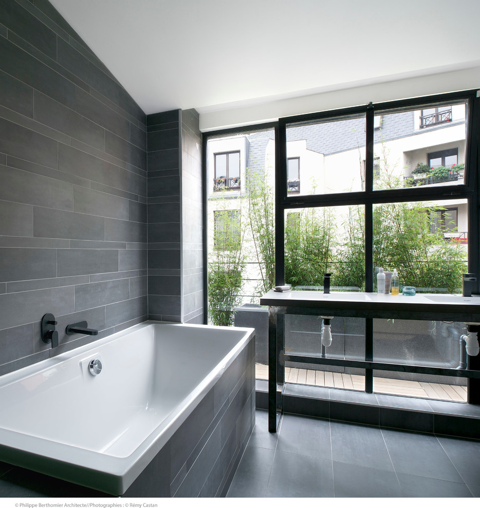 This is an example of a mid-sized contemporary master bathroom in Paris with a console sink, a drop-in tub, gray tile, grey walls, slate floors and slate.