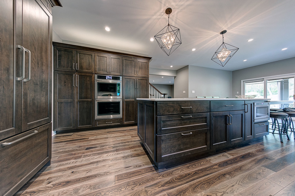Inspiration for a large transitional l-shaped medium tone wood floor and brown floor eat-in kitchen remodel with an undermount sink, flat-panel cabinets, dark wood cabinets, marble countertops, white backsplash, ceramic backsplash, stainless steel appliances, an island and white countertops