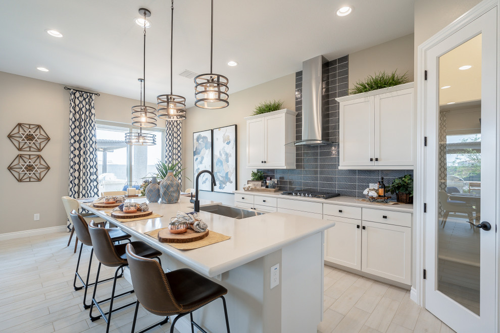 Mid-sized contemporary l-shaped eat-in kitchen in Phoenix with a farmhouse sink, recessed-panel cabinets, white cabinets, solid surface benchtops, grey splashback, ceramic splashback, stainless steel appliances, light hardwood floors, with island, beige floor and white benchtop.