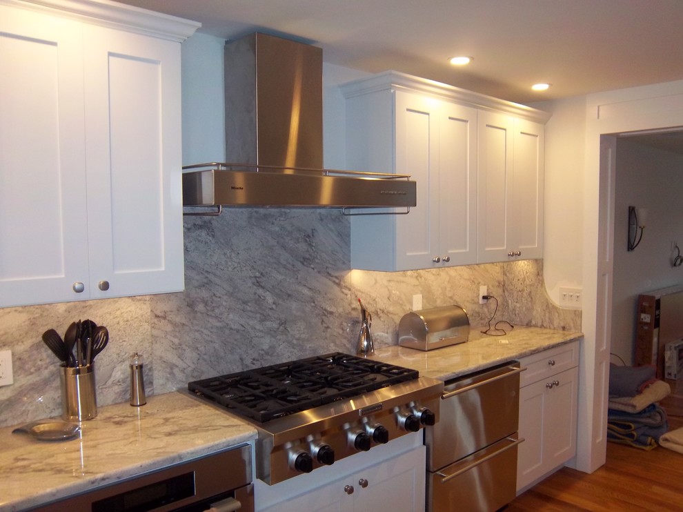 Inspiration for a mid-sized transitional l-shaped medium tone wood floor and brown floor open concept kitchen remodel with an undermount sink, recessed-panel cabinets, white cabinets, granite countertops, gray backsplash, stone slab backsplash, stainless steel appliances and an island
