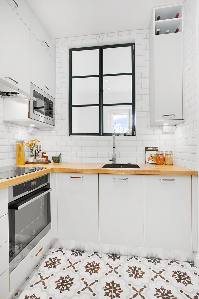 Design ideas for a small scandinavian l-shaped kitchen in Stockholm with a drop-in sink, flat-panel cabinets, white cabinets, wood benchtops, white splashback, subway tile splashback, stainless steel appliances, no island and ceramic floors.