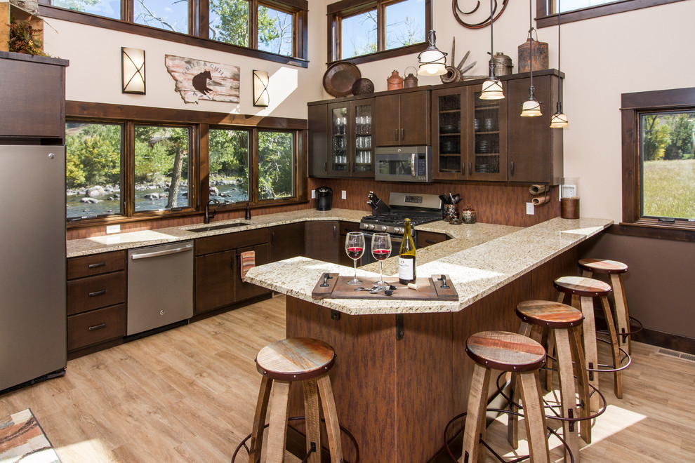 Photo of a country u-shaped open plan kitchen in Other with flat-panel cabinets, dark wood cabinets, stainless steel appliances, light hardwood floors and a peninsula.