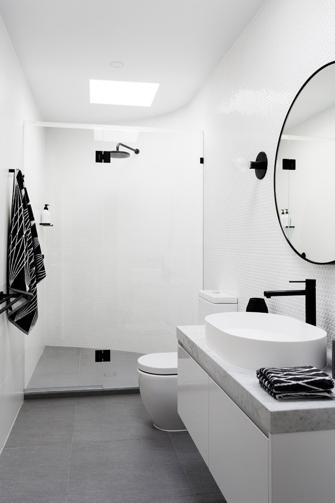 Mid-sized contemporary 3/4 bathroom in Melbourne with flat-panel cabinets, white cabinets, an alcove shower, a one-piece toilet, white tile, mosaic tile, white walls, porcelain floors, a vessel sink, marble benchtops, grey floor, a hinged shower door and grey benchtops.